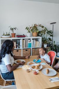 Mother and child sharing a cozy dinner at home, surrounded by plants and books.